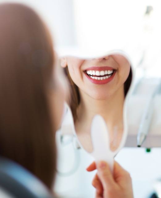 Woman looking at smile in mirror after cosmetic dentistry