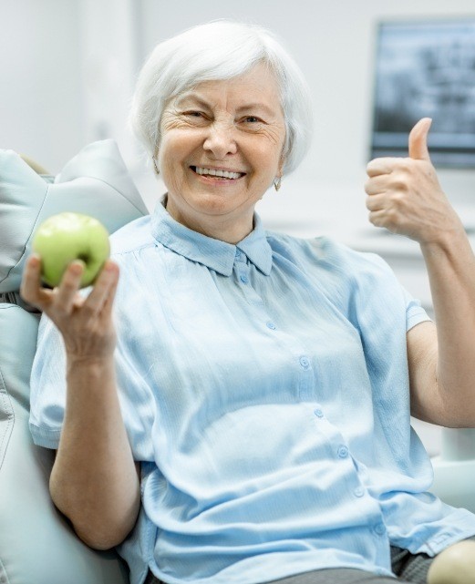 Smiling woman with dentures holding a green apple