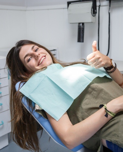 Woman giving thumbs up while receiving dental care