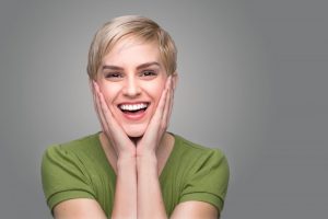 Smiling woman with beautiful teeth putting her hands on her face