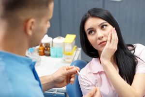 Woman in dental chair holding cheek