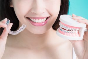 a woman holding clear braces and a mold of traditional braces