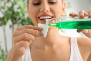 a young woman pouring mouthwash into a cup to rinse her mouth