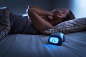 Person with sleep apnea in Spring Lake lies awake next to alarm clock