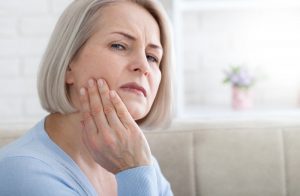 an older woman holding her jaw and wincing in pain