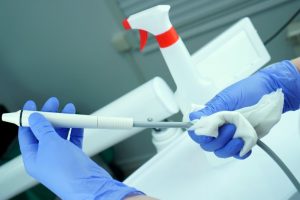 a dental team member using disinfectant to thoroughly clean a piece of equipment